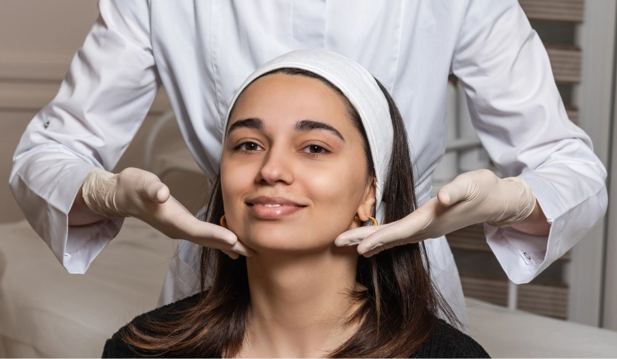 Un profesional con guantes examina el rostro de una paciente, enfocándose en la definición de la mandíbula y el mentón para planificar un tratamiento de armonización facial personalizado.