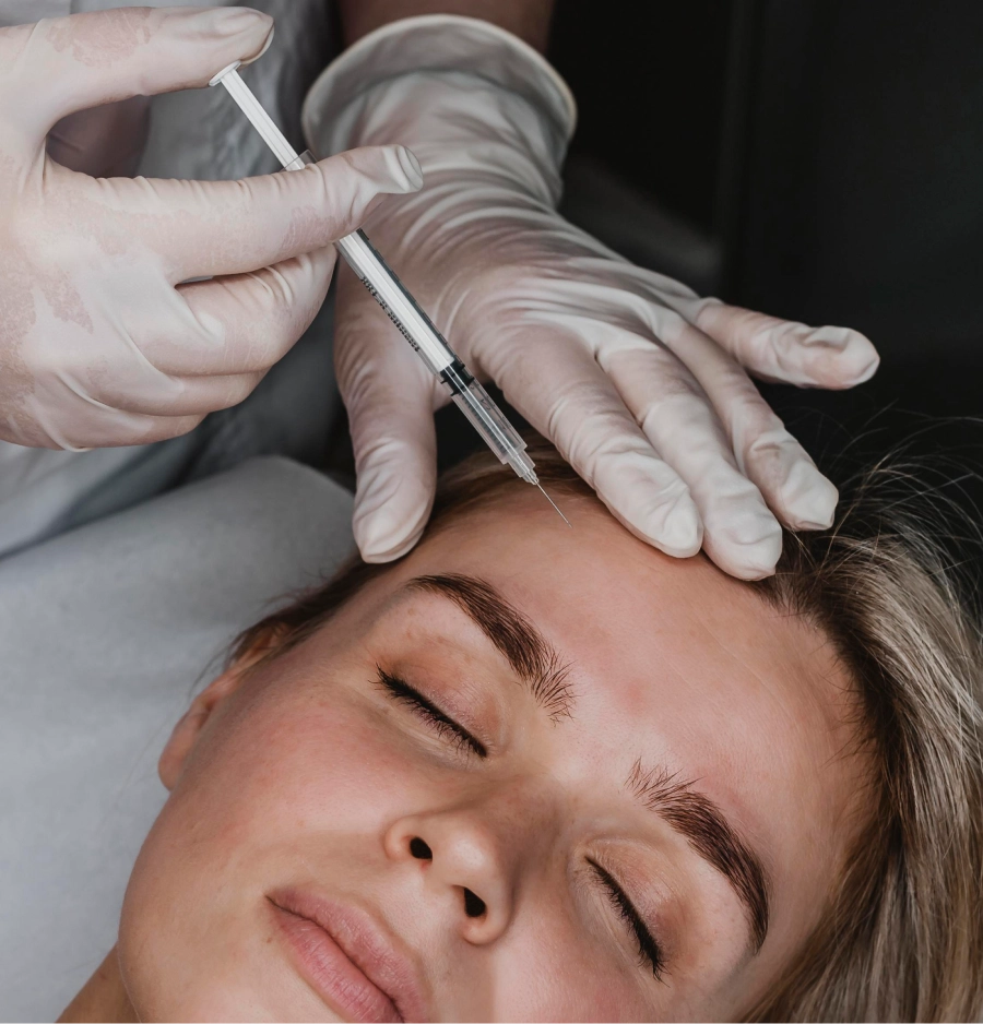 Primer plano de un procedimiento inyectable de alta precisión en la frente. Un profesional con guantes blancos realiza una aplicación estratégica para suavizar arrugas dinámicas y restaurar la frescura del rostro.